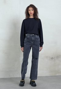 Top de algodão preto de mangas compridas combinado com jeans de denim cinza escuro de cintura alta. Sapatos plataforma pretos robustos com detalhes em corrente realçam o conjunto.