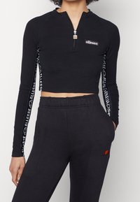 Black cropped long-sleeve top with a half-zip front, featuring branding along the sleeves and a fitted design. Paired with black joggers.
