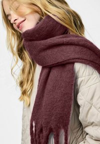 Bordeaux tørklæde lavet af blødt, struktureret stof med frynser i enderne, båret over en lysfarvet quiltet jakke.