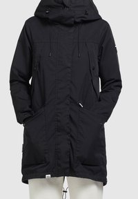 Svart huva jacka med dragsnören, knappade fickor och mittlång design. Tillverkad av texturerat tyg med en stilren och funktionell look.