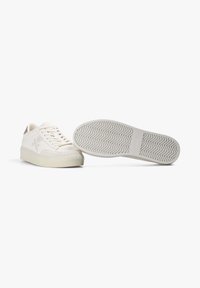 Zapatillas deportivas blancas de caña baja con cordones, punteras reforzadas y suelas de goma con un patrón en zigzag, exhibidas sobre un fondo blanco.