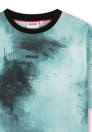 T-shirt turquoise clair avec des motifs abstraits sombres, col rond noir et logo "HUGO" en noir à l'avant. Texture douce.