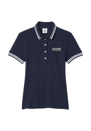 Polo Lacoste azul marino con cuello y mangas a rayas blancas, tapeta de botones y texto "Lacoste Roland Garros Club" en el pecho.