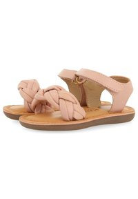 Sandalias de cuero trenzado rosa con suela plana y tira en el tobillo, que cuentan con un detalle de metal dorado y una plantilla suave y texturizada.