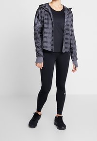 Musta urheiluasu, joka sisältää vetoketjullisen hupparin, jossa on "NIKE AIR" -teksti, tiukan mustan yläosan ja mustat legginsit. Kengät: mustat urheilujalkineet.