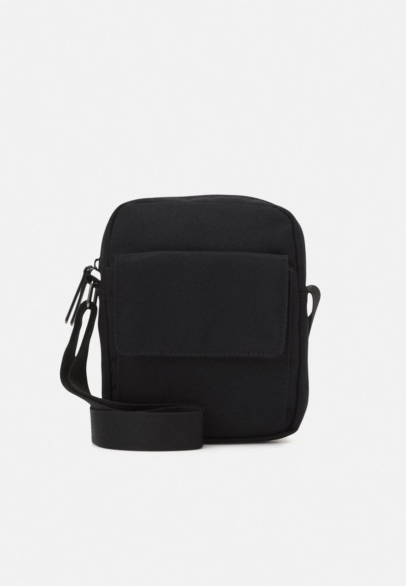 Sac bandoulière en tissu noir avec poche avant à rabat et sangle d'épaule réglable sur fond blanc.