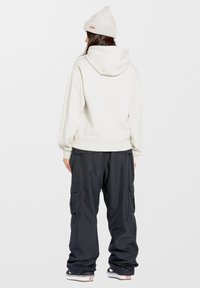 Lichtgrijze hoodie met een ontspannen pasvorm, gecombineerd met donkere cargobroeken met zijzakken en elastische boorden. Een beanie voegt textuur toe.