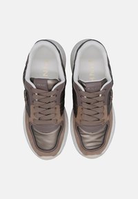 Sneaker marrone e grigio con una parte superiore liscia e lucida e accenti in suede testurizzato. Presenta una suola bianca spessa e lacci piatti. Logo dorato sulla linguetta.