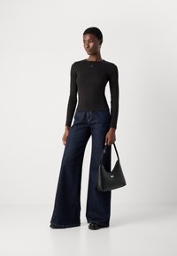 Black long-sleeve top, fitted, paired with wide-leg dark blue denim jeans. Accessorized with a black leather handbag featuring a logo detail.
