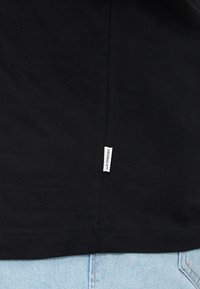 Sort bomulds t-shirt med korte ærmer, med et lille "ORIGINALS" mærke syet på venstre side. Glat tekstur og klassisk snit.