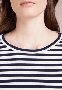 Kortärmad t-shirt med rund hals och marinblå och vita horisontella ränder. Tyget verkar mjukt med en slät textur och slitstarka sömmar.