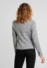 Grau gestreifter Blazer mit taillierter Passform, strukturierten Schultern und geknöpften Manschetten. Das Material ist gewebter Stoff mit einer strukturierten Oberfläche.