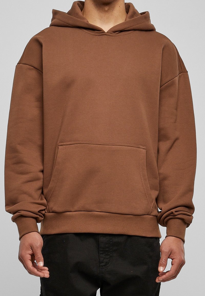 Brun hoodie gjord av mjukt, strukturerat tyg. Har en kenguruficka, lös passform och ribbade ärmslut. Enkelt utformad med huva.