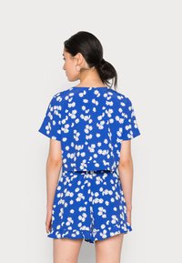 Top curto floral azul e calções combinando com padrão de margaridas. Manga curta, ajuste descontraído, tecido leve com uma bainha de babados.
