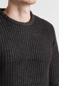 Donkergrijze gebreide trui met een geribbelde textuur, voorzien van een ronde halslijn en lange mouwen.