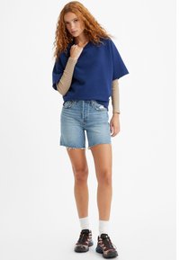 Top corto de manga corta en color navy, de corte holgado, combinado con pantalones cortos de mezclilla de cintura alta con dobladillo deshilachado. El calzado presenta zapatillas deportivas oscuras con detalles en color.