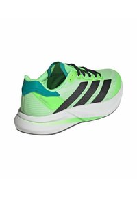 Zapatilla atlética de malla verde con rayas negras, acentos turquesa y una suela blanca ligera, que presenta una parte superior texturizada y un sistema de cordones.