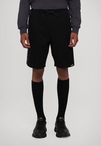 Shorts sportivi neri realizzati in tessuto morbido, con vita regolabile tramite coulisse e grafiche stampate sui lati. Abbinati a calze nere al ginocchio.