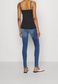 Top negro de tirantes finos, vaqueros ajustados azules con lavado degradado y zapatos ligeros sin cordones con suela negra. Diseño sencillo y textura suave.