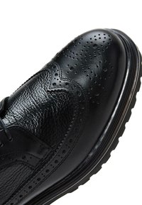 Zwarte leren dresschoenen met brogue-details, een textuurafwerking, ronde neus en een contrasterende zwarte rubberen zool.