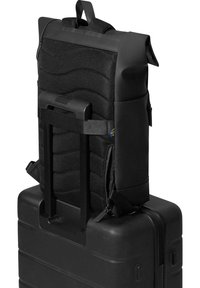 Black backpack with textured nylon backrest and adjustable straps, mounted on a solid black luggage case with a retractable handle.