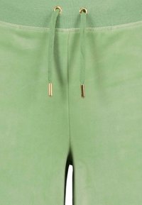 Pantalons de survêtement verts avec une texture douce, dotés d'un cordon de serrage avec des embouts en métal doré et d'une ceinture lisse. Vue en gros plan.