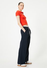 Rød kortærmet polo-shirt med en cropped design, parret med løstsiddende navy bukser med snørelukning og sidelommer.