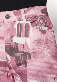 Pantalon en denim rose avec un imprimé en collage, détails en noir et blanc, design à cinq poches et fermeture à bouton argenté.