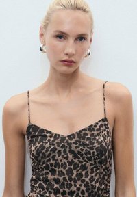 Haljina sa leopard printom od mekog materijala, s tankim naramenicama i krojem koji prati liniju tijela, s naborima na struku. Srebrne kružne naušnice.