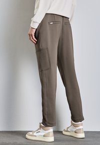 Pantalons de survêtement marron au coupe ample, dotés de poches latérales, d'une texture lisse et de détails cousus. Associés à des baskets montantes beige.