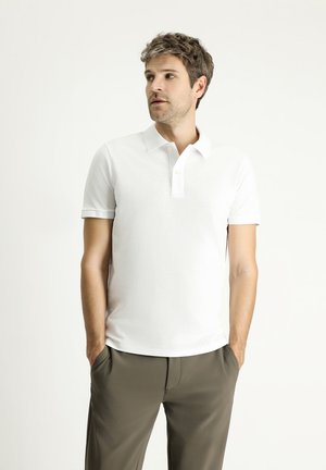 Camisa polo blanca con un acabado texturizado, cuello clásico, manga corta y cierre de dos botones, combinada con pantalones oscuros de color oliva.