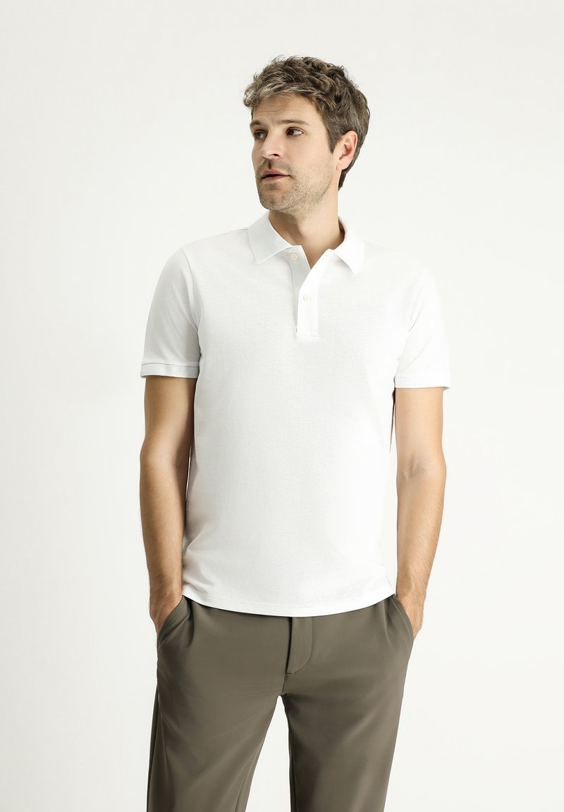 Polo bianco con finitura testurizzata, colletto classico, canonico con due bottoni e maniche corte, abbinato a pantaloni verde oliva scuro.