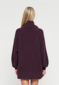 Pull oversized en maille côtelée de couleur violet profond. Il présente un col montant et des manches larges, fabriqué en matière tricotée douce et texturée.