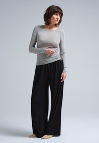 Graues Langarmshirt mit einer figurbetonten Passform, kombiniert mit einer lockeren schwarzen Hose. Das Ensemble zeichnet sich durch einen weichen Stoff und eine lässige Silhouette aus.