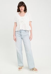 Haut péplum floral blanc avec des manches courtes bouffantes et un décolleté carré, associé à un jean large bleu clair et des sandales épaisses.