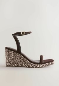 Sandalo wedge in suede marrone con cinturino alla caviglia, dotato di una suola in tessuto a spina di pesce intrecciato e una superficie superiore liscia e leggermente lucida.