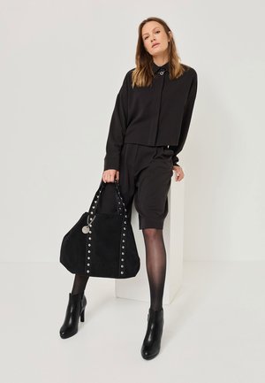 Borsa tote in suede nero con borchie argentate sui lati, dotata di doppi manici e un charm decorativo. Texture liscia e design capiente.