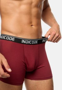 Boxeri maronii cu talie elastică neagră, având numele brandului "INDICODE" imprimat în alb. Material moale, elastic, cu un design ajustat.