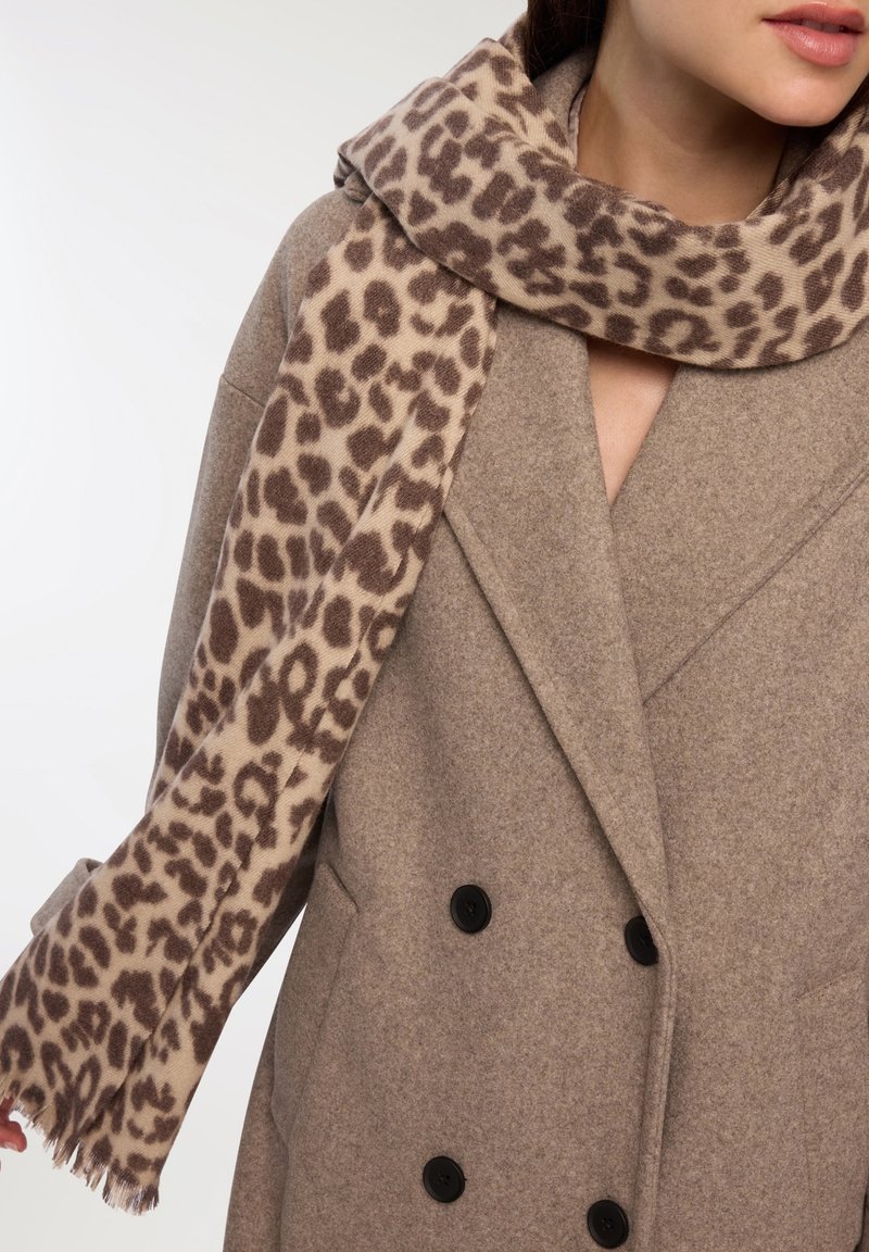 Szalik w leoparda w jasnym beżu i brązie, wykonany z miękkiego materiału, zarzucony na szary płaszcz z podwójnymi guzikami i teksturowanym materiałem.