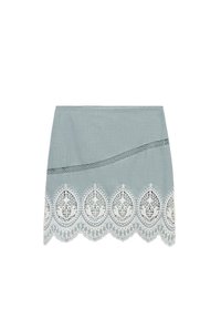 Jupe bleu clair avec bordure en dentelle aux bords festonnés, motifs complexes et ligne décorative horizontale traversant le tissu.