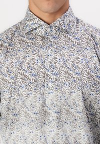 Knappskjorte i lys grå med et blomsterdesign som har blå blomster og grå blader. Glatt tekstur og standard kragedesign.