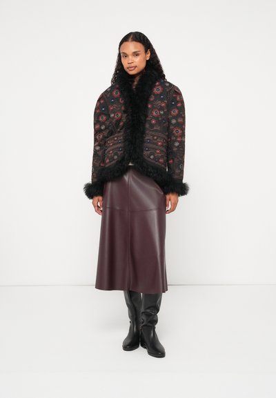 Črna prešita jakna s cvetličnim vzorcem, ovratnikom in manšeti iz umetnega krzna, v kombinaciji z burgundskim usnjenim krilom in črnimi škornji do kolen.