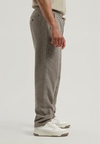 Grijze geruite broek van geweven stof, met een elastische tailleband met trekkoord, zijzakken en een losse pasvorm. Witte sneakers zichtbaar.