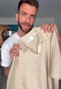 Beige pletená polo košile s velkým síťovým vzorem, límečkem a krátkými rukávy. Štítek viditelný na vnitřní straně límce.