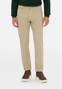 Chinos beige de corte recto, con un diseño clásico de cinco bolsillos. Llevados con zapatillas marrones que presentan cordones burdeos.