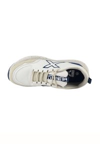 Zapatilla deportiva blanca y azul marino con malla y materiales sintéticos en capas, punta redonda, diseño de cordones y detalle del logotipo en la lengua con patrón.