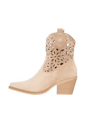 Beige suède enkellaars met blokhak en een bloemen uitsnijding patroon op het bovenste deel, met een puntige neus en een aantrekkoord.