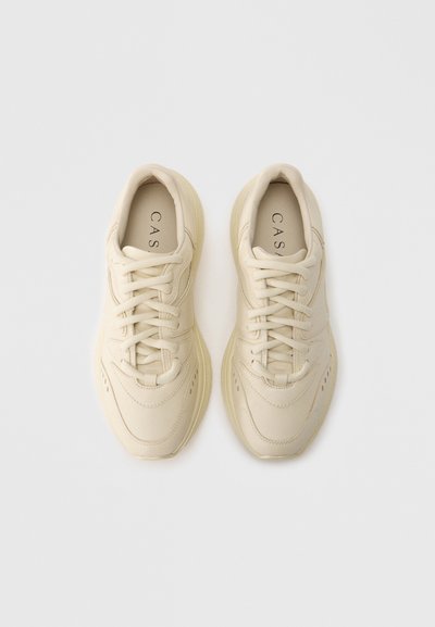 Μπεζ αθλητικά παπούτσια με λείο δερμάτινο επάνω μέρος, στρογγυλεμένη μύτη, σχέδιο με κορδόνια και υφή διακοσμητικών στοιχείων. Ετικέτα στο εσωτερικό με την ένδειξη "CAS."
