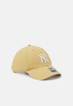 Casquette en coton jaune avec un logo "NY" brodé en blanc, visière courbée et une étiquette de taille sur le panneau avant. Tissu texturé avec des détails de couture.