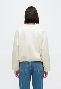 Krémový pulóver s voľným strihom, zaobleným výstrihom a rebrovaným lemom. Má mäkkú, hladkú látku a prepadnuté ramená.